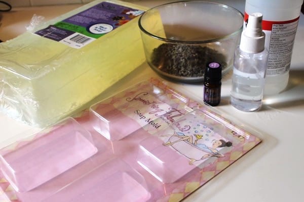 soap base block, dried lavender, bottle of lavender essential oil, spay bottle of alcohol and soap mold to make a simple lavender soap recipe